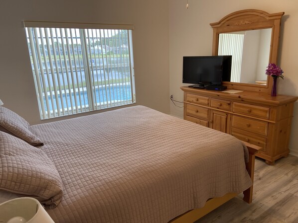Un dormitorio con cama, cómoda, televisor y ventana con persianas.