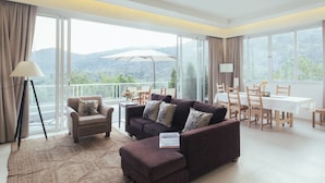 Una sala moderna con un sofá, un sillón y un otoman, un comedor con mesa y sillas, y ventanas amplias con vistas a las montañas.