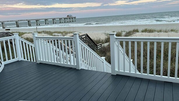 A wooden deck with white railings overlooking a beach and a pier.