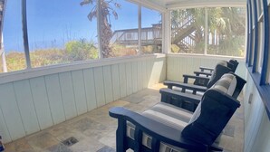 A covered patio with stone flooring and wooden furniture.