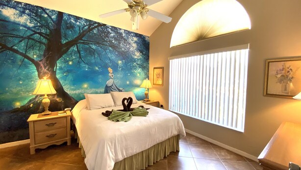 Quarto com um grande mural de uma paisagem florestal, uma cama com roupa de cama branca, duas mesas de cabeceira com abajures e um ventilador de teto.
