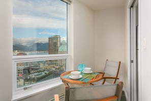 Ein Balkon mit Tisch für zwei Personen, einem Stuhl und Blick auf eine Stadtlandschaft mit Gebäuden und Bergen.