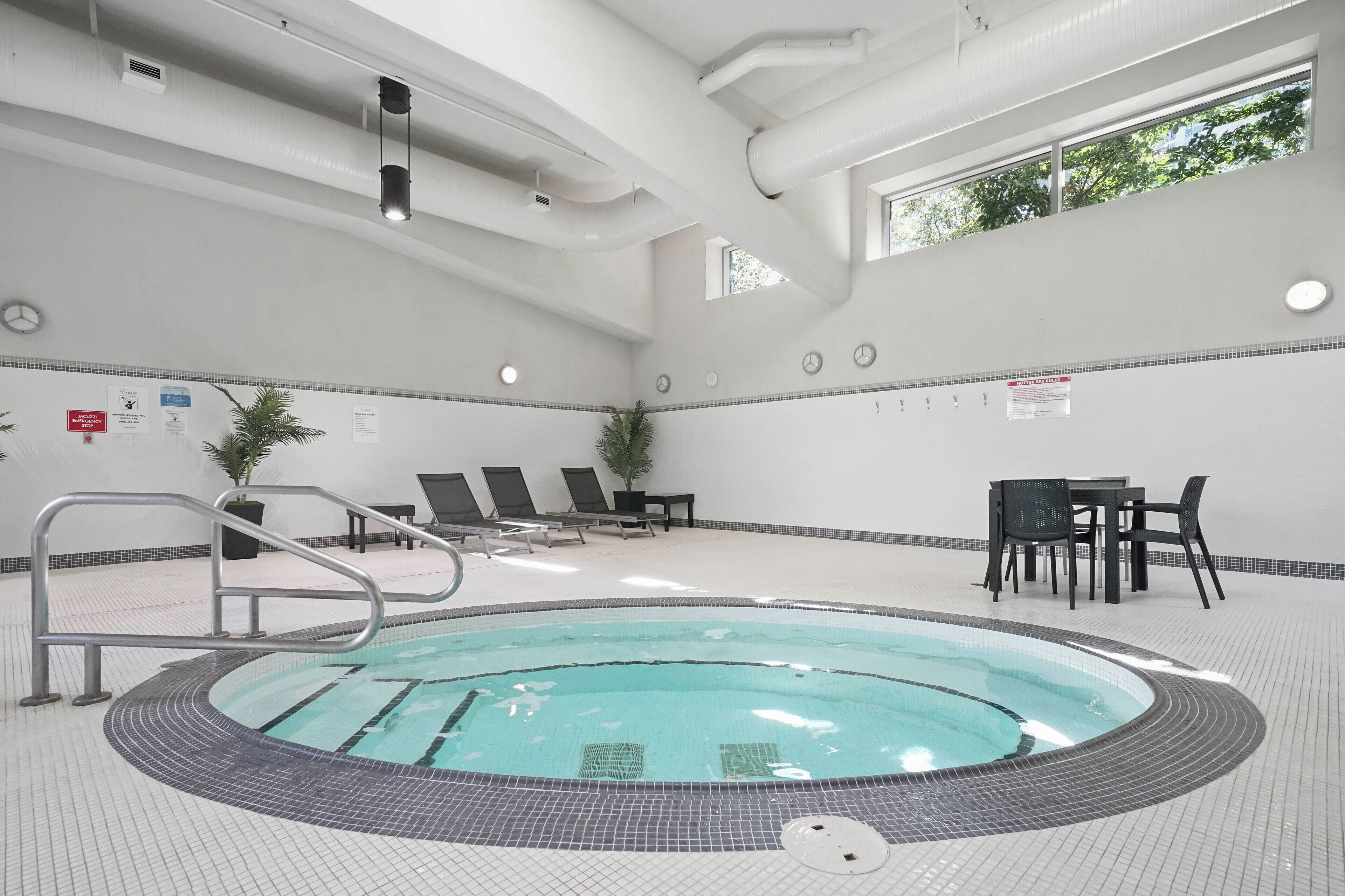 Piscina com borda azulejada, espreguiçadeiras e mesa com cadeiras.
