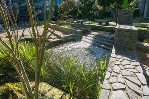 Ein Steinkonstruktion mit Wasserlauf und Stufen, umgeben von Pflanzen und Steinmauern.