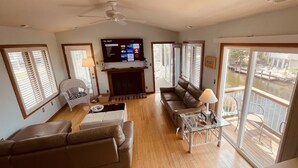 A living room with a fireplace, a television, and a balcony with a view of a body of water. - Private Canalfront House, Dock, Deck, Fire Pit, Parking, 7th house to the Beach (South Bethany Beach)