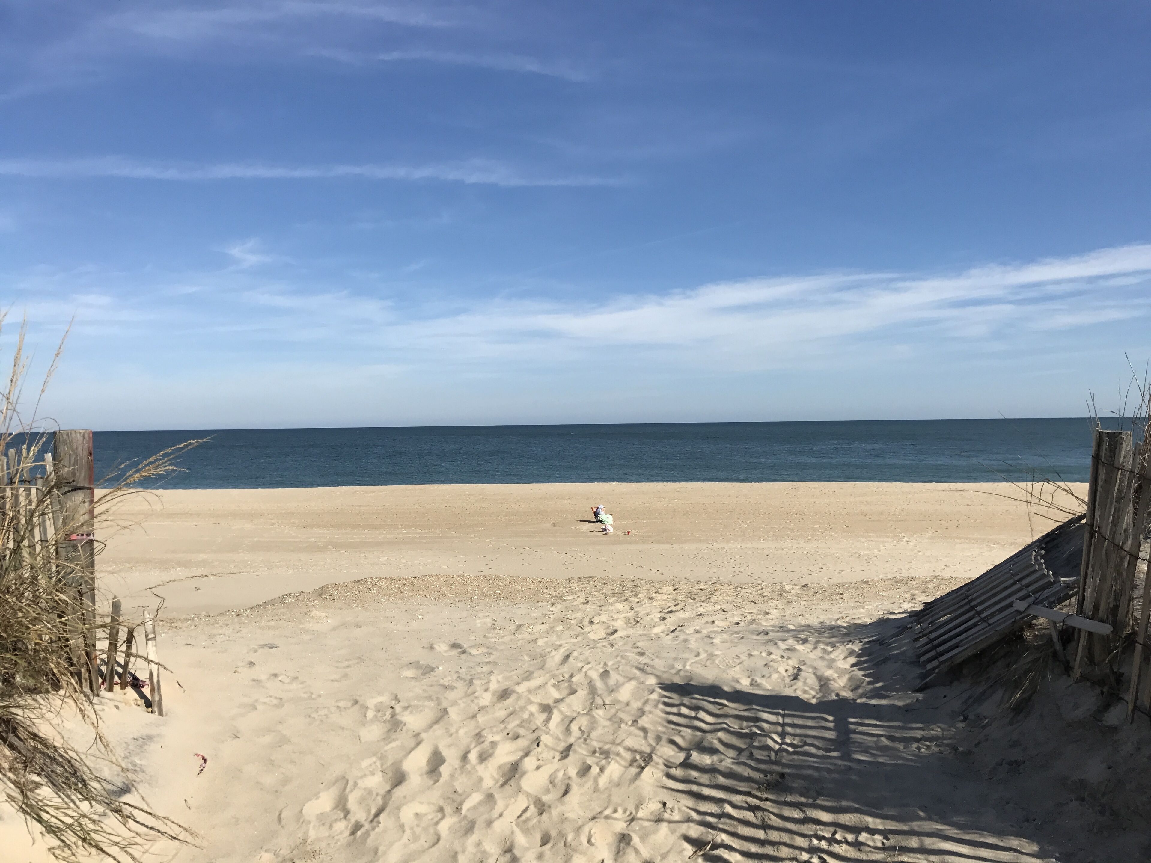 Une plage de sable bordée d’une clôture en bois, offrant une vue dégagée sur l’océan.