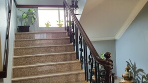 A staircase with a wooden handrail and black balusters, leading to a landing area with a decorative wall piece and potted plants. - Hotel Butsugen (Kathmandu)