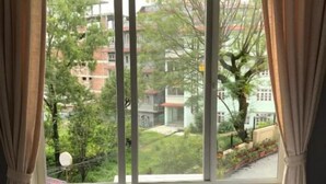 A hotel room with a large window, curtains, a bed, and an air conditioning unit. - Hotel Butsugen (Kathmandu)