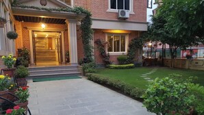 A brick building with a well-maintained garden, a welcoming entrance with steps, and potted plants. - Hotel Butsugen (Kathmandu)