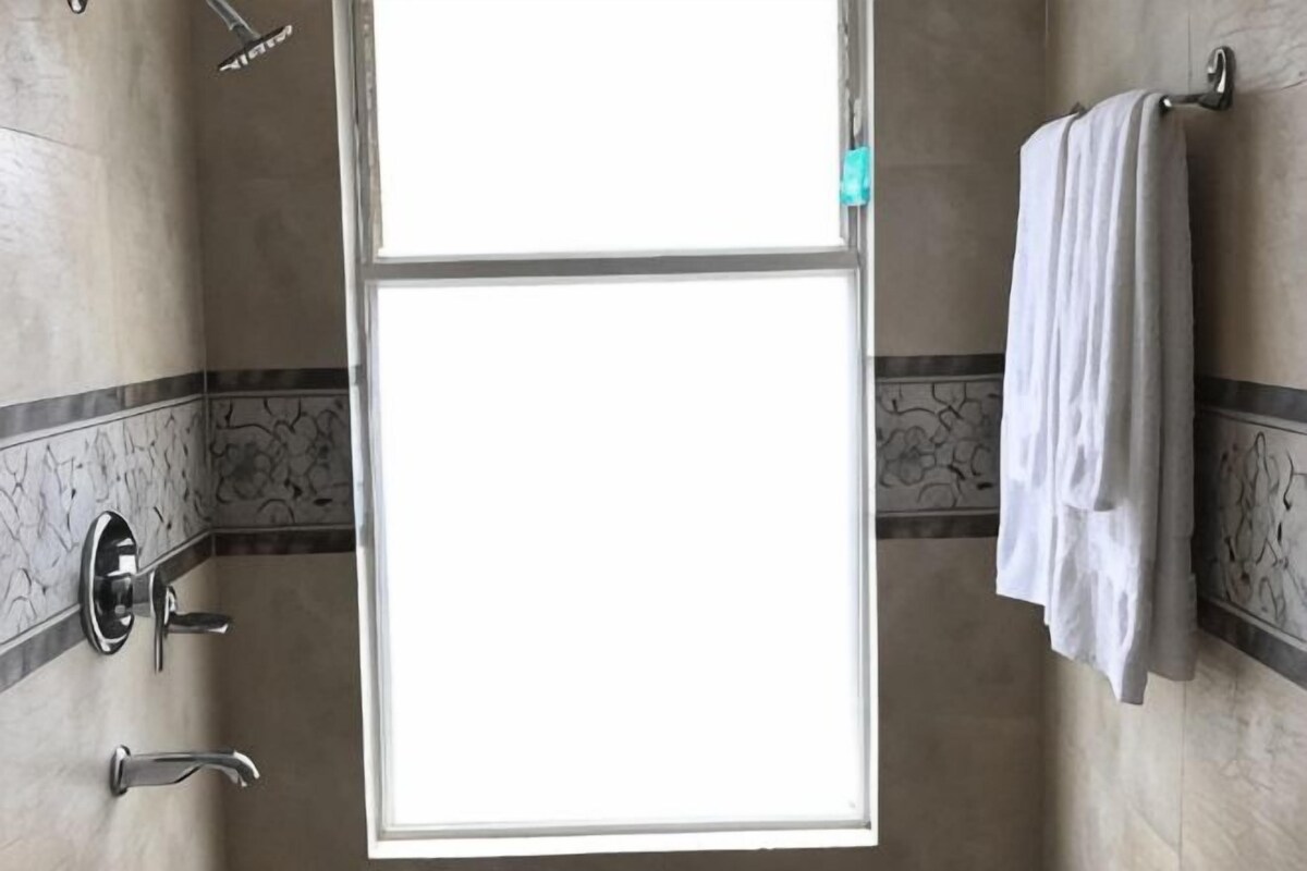 A bathroom with a shower, a towel rack, and a window.