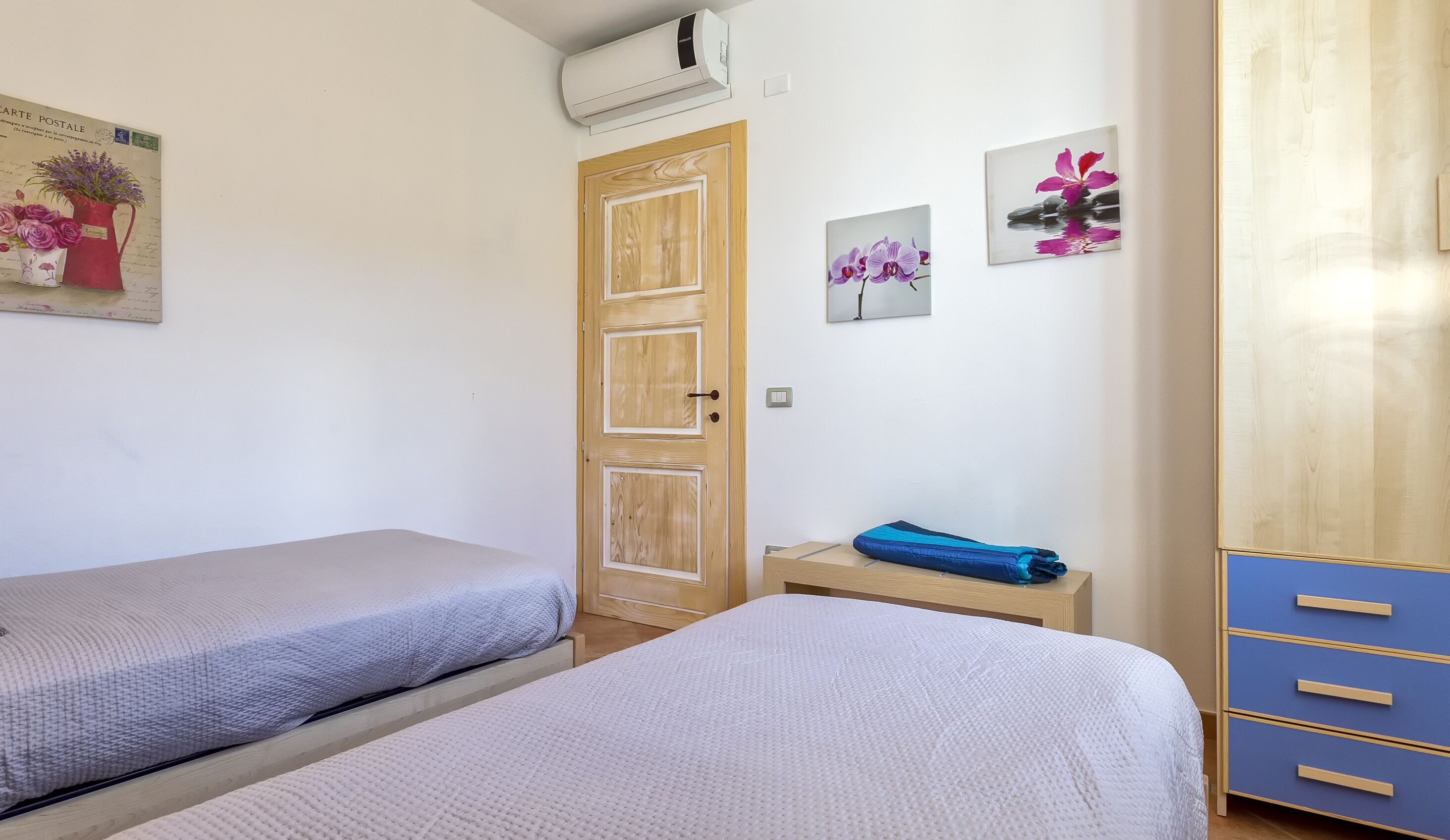 Un dormitorio con dos camas individuales, un armario de madera y una mesita con un objeto doblado.