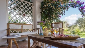 An outdoor patio with wooden furniture, a table with food and drinks, and a view of greenery. - Spectacular Villa with independent pool for 8 people near the beach (Alghero Italy)