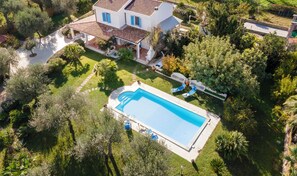 Vista aérea de una casa con piscina, rodeada de exuberante vegetación y un jardín cuidado.
