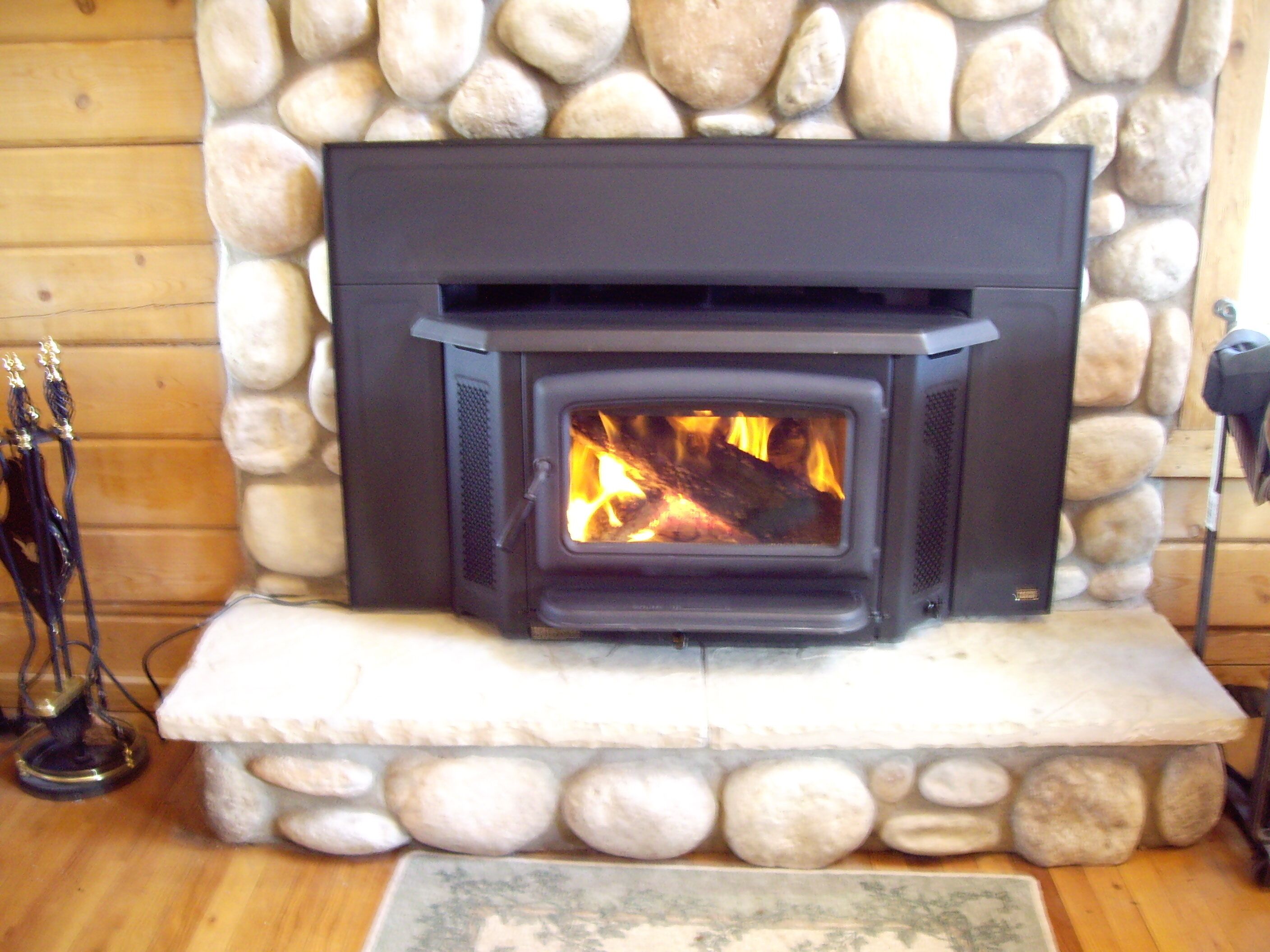 Una chimenea de piedra con frente negro, un repisa y fuego encendido en su interior.