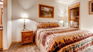 Un dormitorio con una cama, dos mesitas de noche, una mesilla auxiliar, una ventana y un cuadro en la pared.