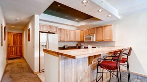 Una cocina moderna con armarios de madera, una isla central con taburetes de bar, un refrigerador y un microondas.