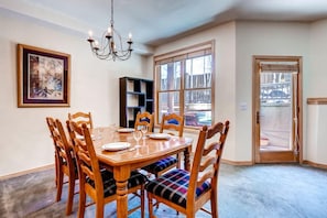 A dining room with a wooden table and chairs, a chandelier, a bookshelf, and a large window.