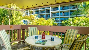 A round table with striped chairs on a balcony, overlooking a multi-story building with balconies and lush greenery.