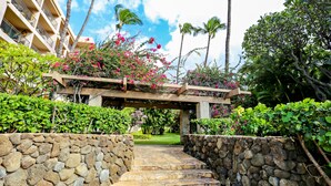 A stone pathway leading to a covered area with a wooden pergola adorned with pink flowers.