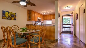 A kitchen with wooden cabinets, a microwave, and a dining area with wicker chairs and a glass table.