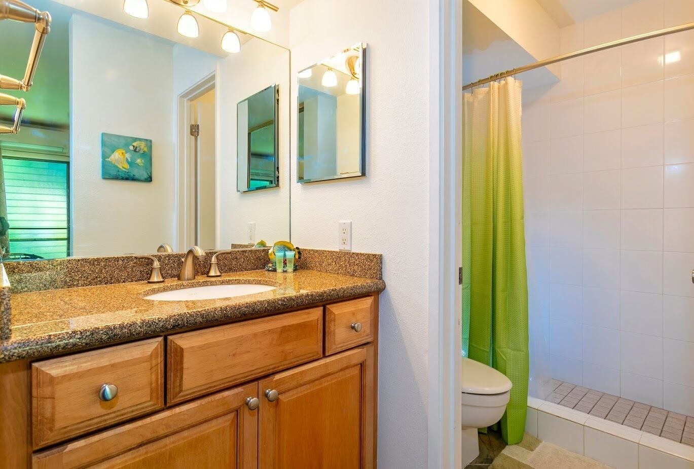Un baño con lavamanos de encimera de granito, armarios de madera, un espejo y una ducha con cortina verde.