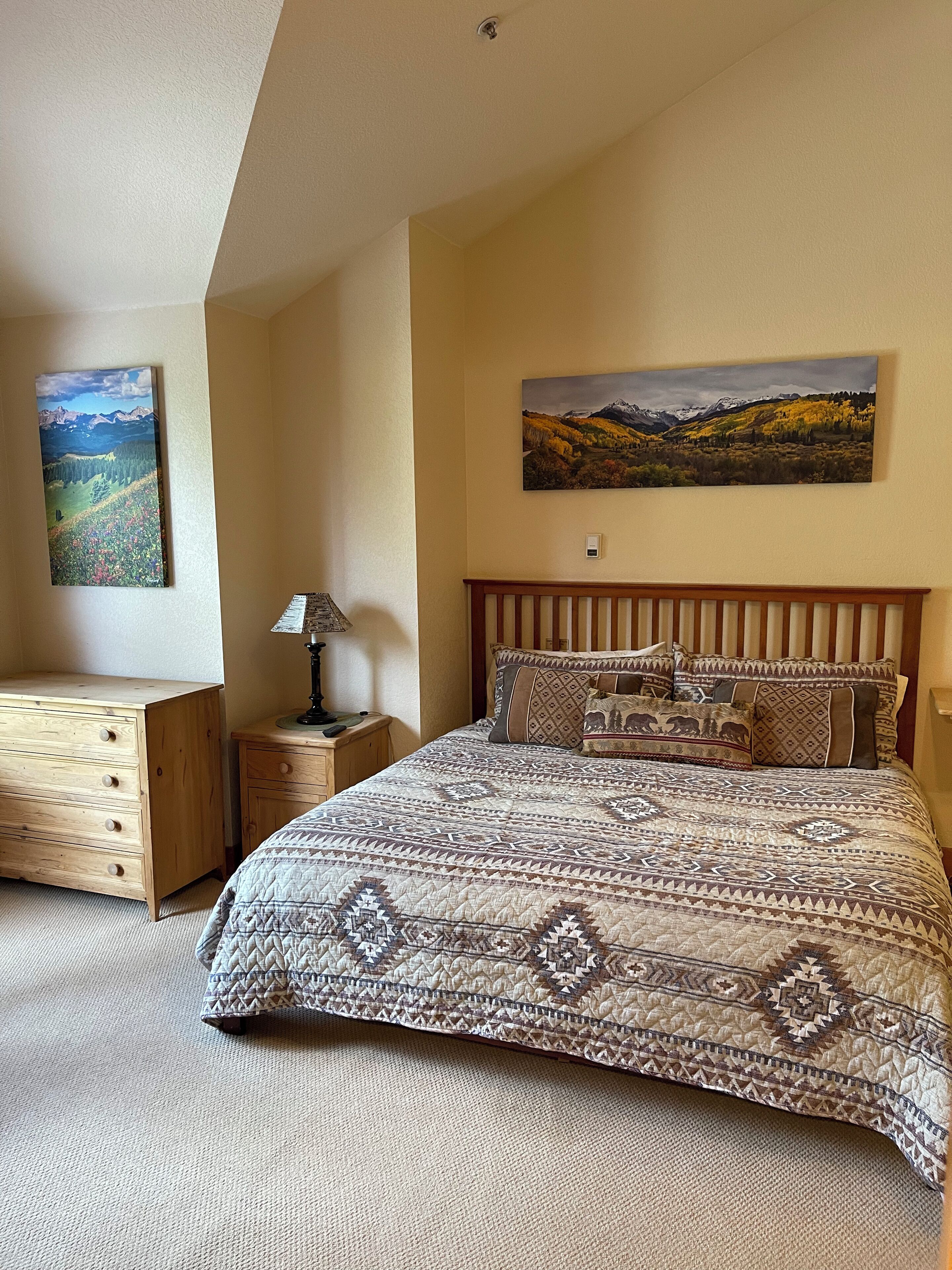 Un dormitorio con una cama grande, un aparador de madera, una mesita de noche y dos cuadros en las paredes.
