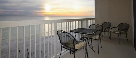 Uma varanda com vista para a praia e para o pôr do sol. Há quatro cadeiras e uma mesa na varanda.