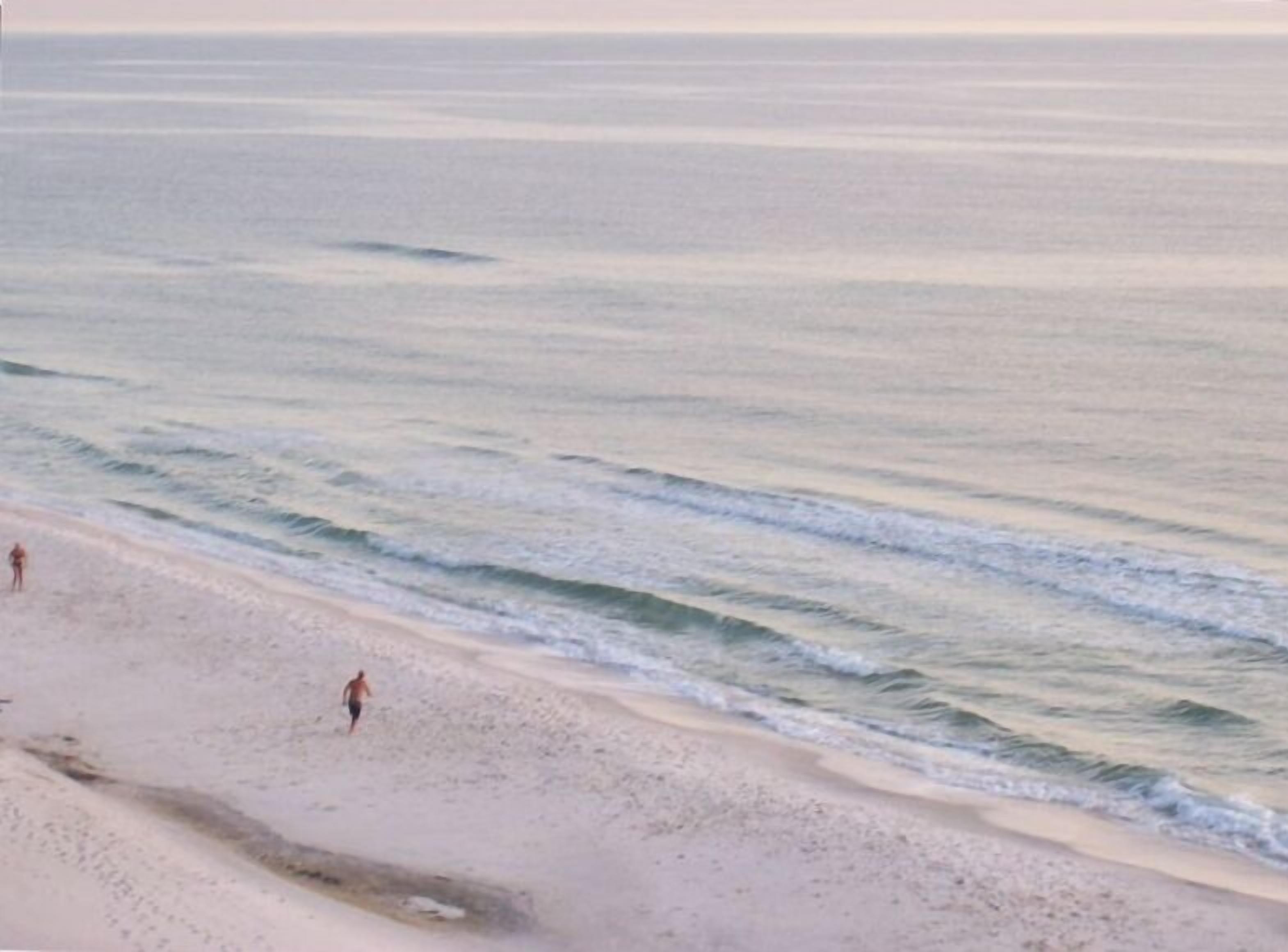 Una playa con dos personas caminando por la orilla.