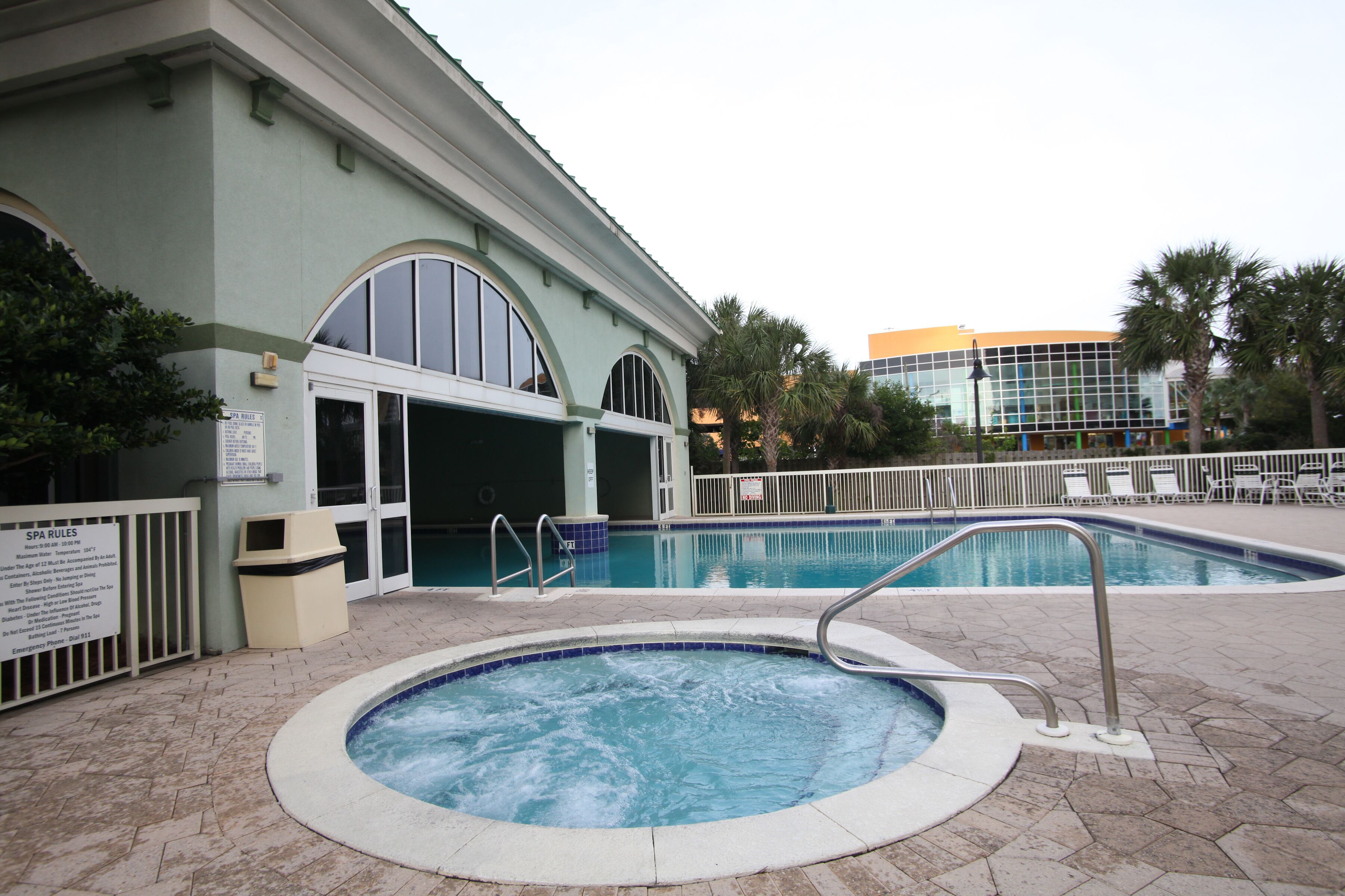 A swimming pool area with a hot tub, a spa, and a building with large windows.