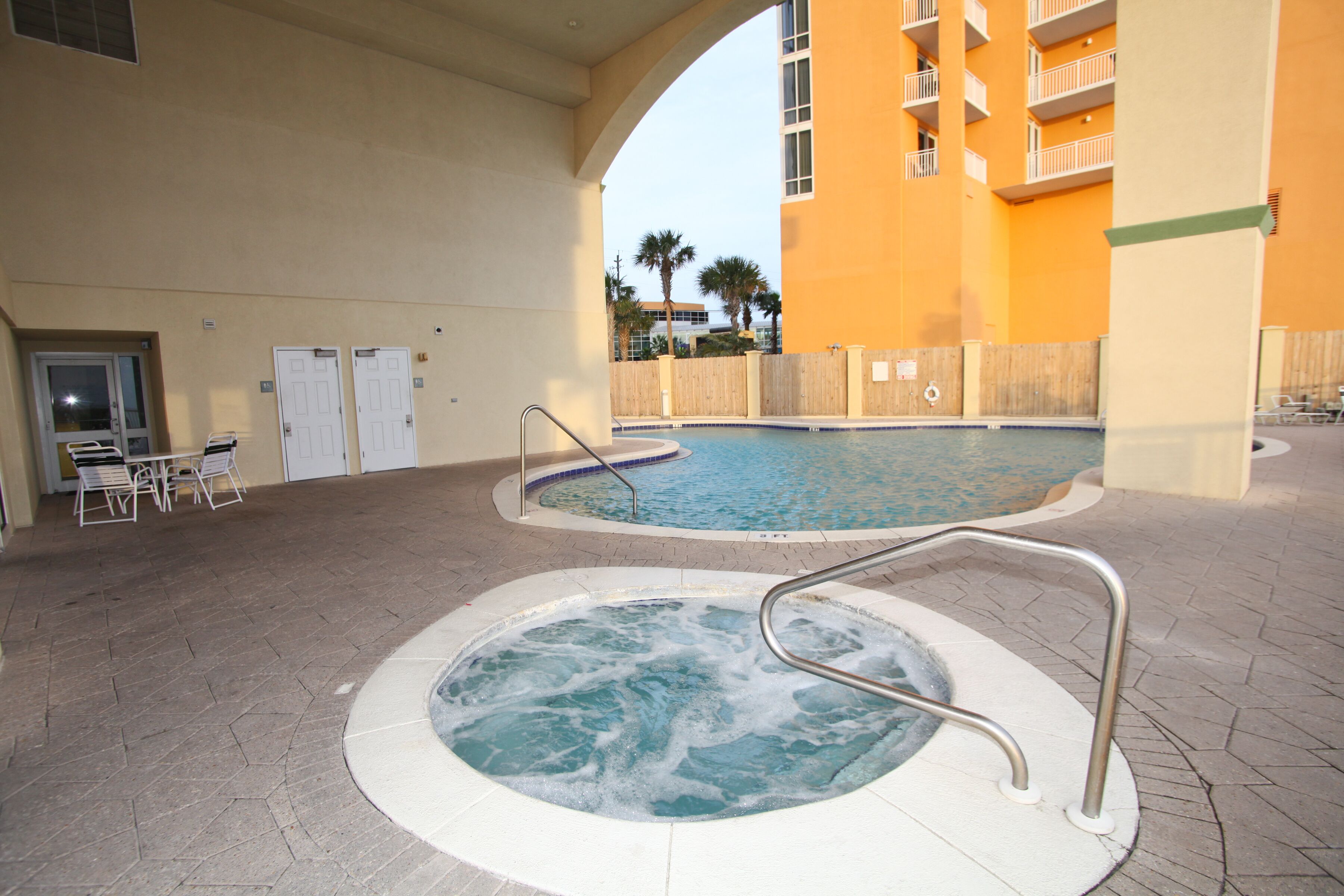 A swimming pool area with a hot tub, lounge chairs, and a covered patio.