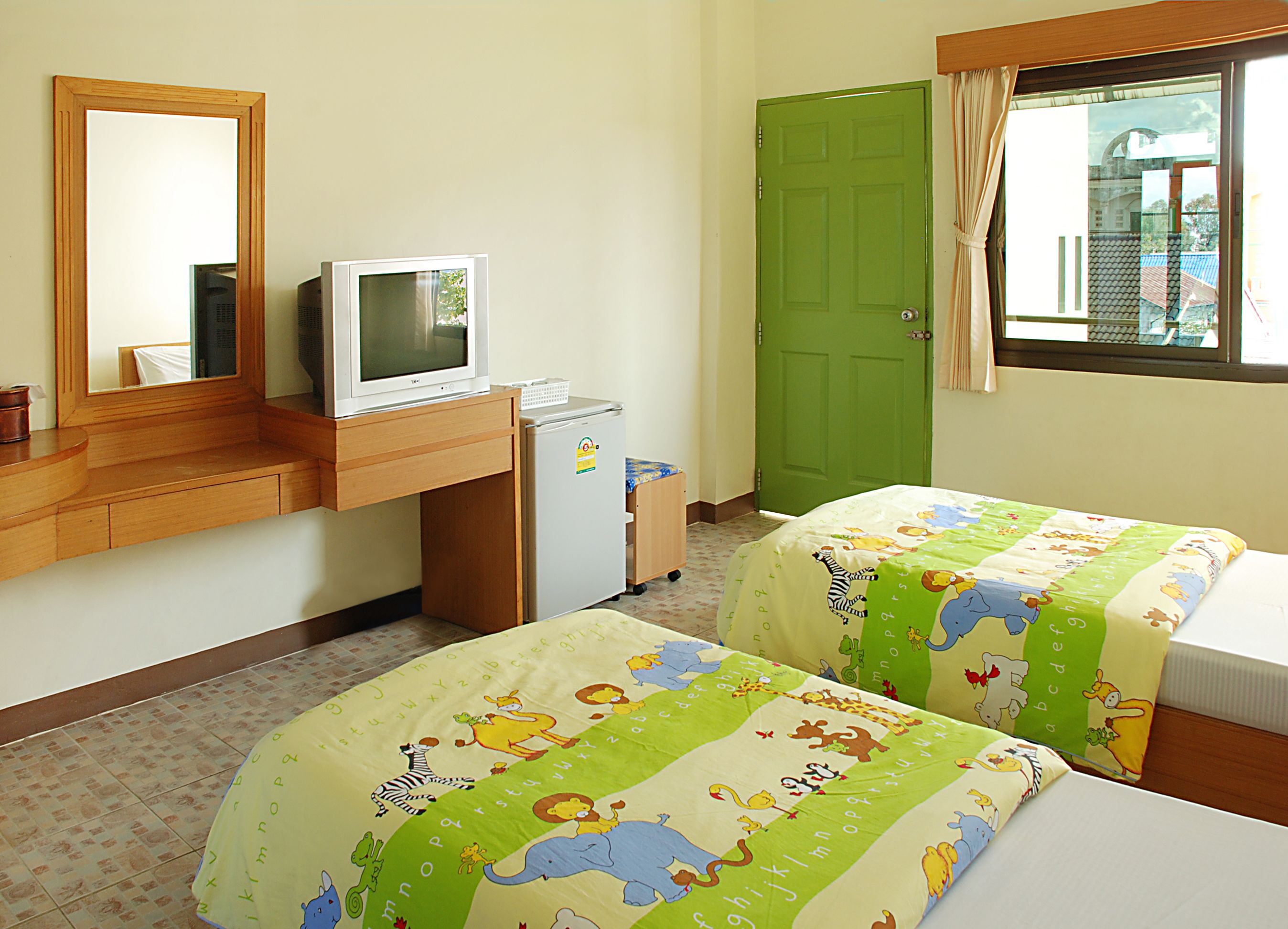 A hotel room with two beds, a television, a refrigerator, a mirror, and a green door.