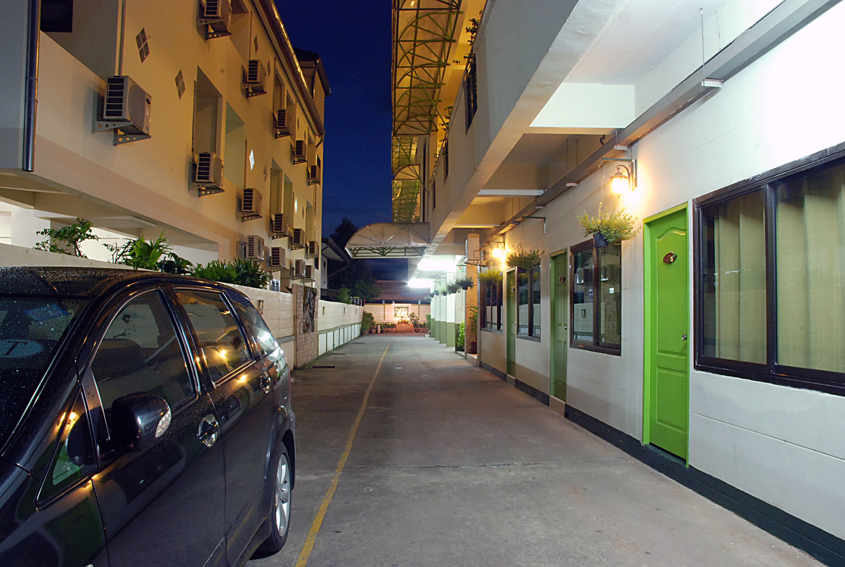 A narrow alleyway with a parked car, buildings on either side, and a green door on the right.