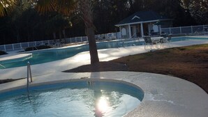 Una piscina con una palmera, sillas de descanso y un pabellón cubierto.
