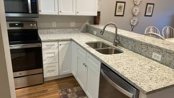 A modern kitchen with stainless steel appliances, white cabinetry, granite countertops, and a built-in dishwasher.