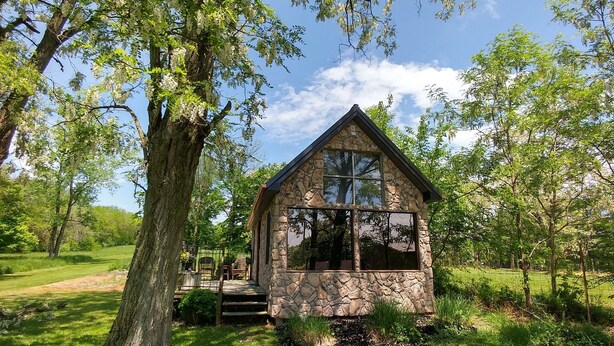 Eine Steinhütte mit einem großen Fenster, umgeben von Bäumen und Gras.