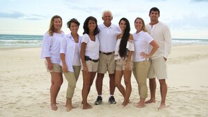 Un grupo de personas de pie en una playa arenosa, con el océano al fondo.