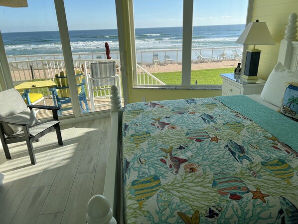 Une chambre avec vue sur l’océan, un lit recouvert d’une couette à motifs de poissons, une chaise et une petite table.