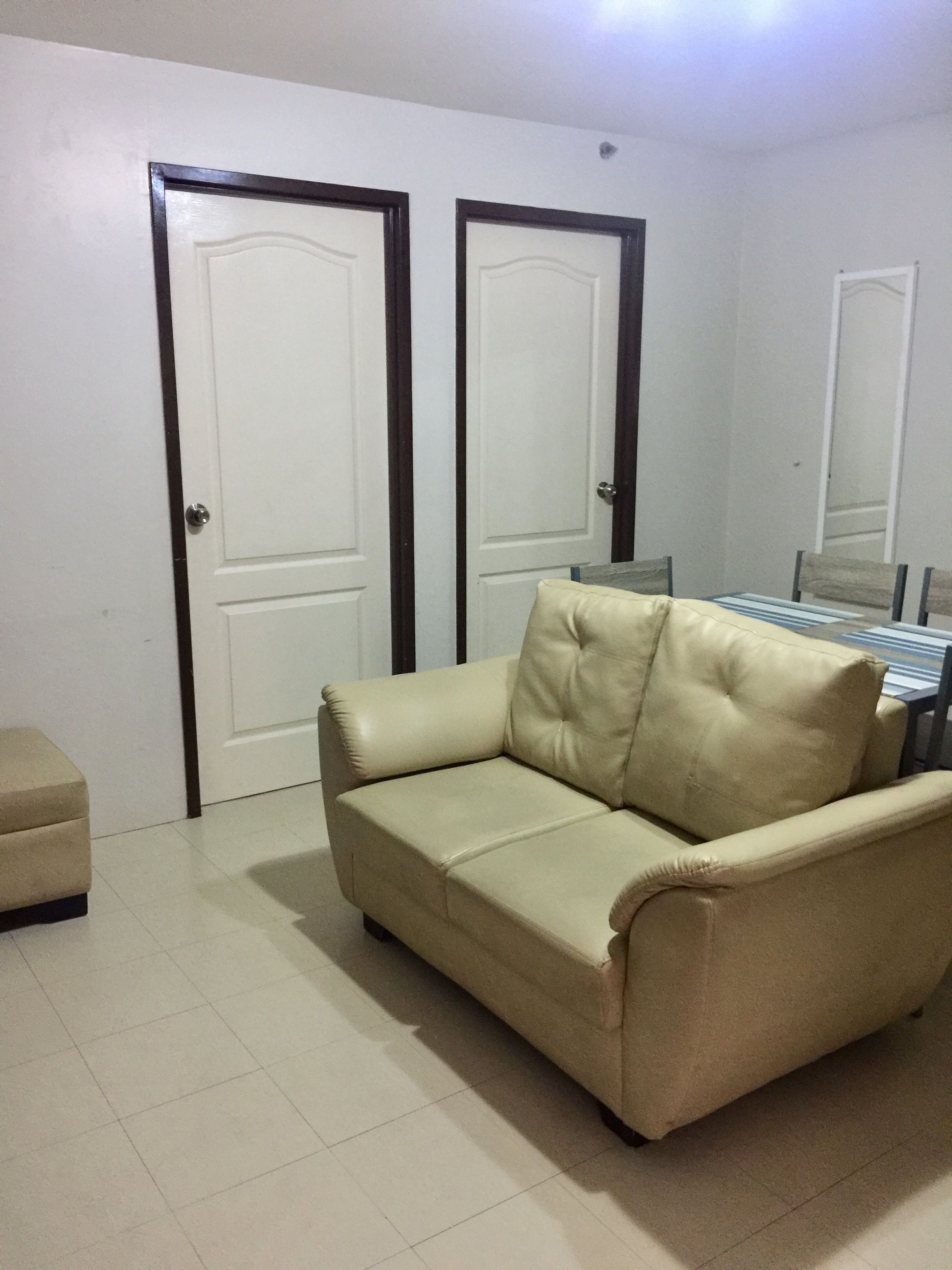 A room with a beige sofa, a small ottoman, and two doors with dark frames.