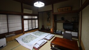 A traditional Japanese room with tatami flooring, a futon bed, a wooden table, a television, and a shoji screen. - Yamadaya Ryokan (Nozawaonsen)