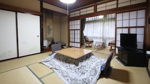 A traditional Japanese room with tatami flooring, a low wooden table, a television, and sliding doors. - Yamadaya Ryokan (Nozawaonsen)