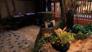 A stone bench, a small table, and a rock with plants in a garden setting. - Yamadaya Ryokan (Nozawaonsen)