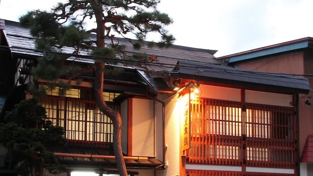 A traditional Japanese building with a wooden gate, a small garden, and a signboard. - Yamadaya Ryokan (Nozawaonsen)