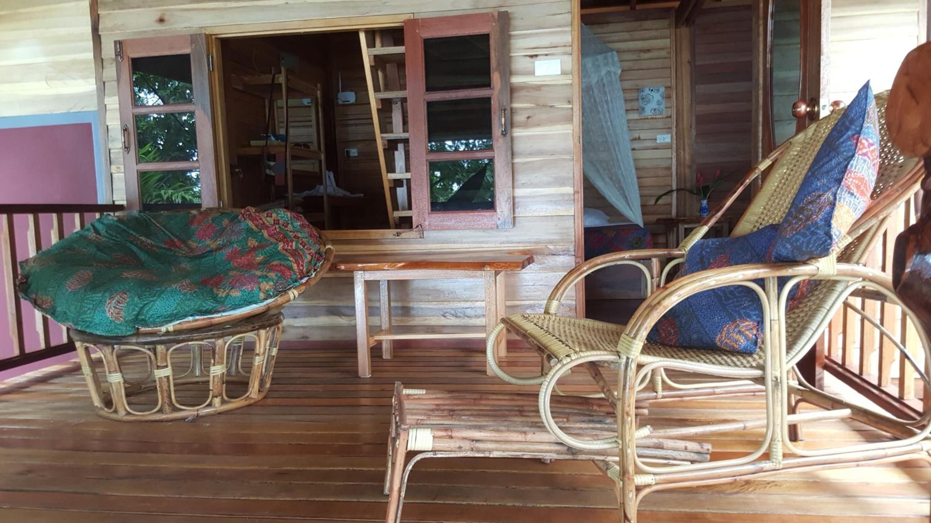 A wooden porch with wicker furniture, including a rocking chair and a cushioned chair.