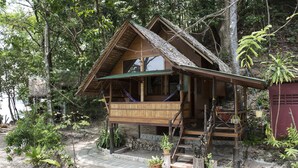Una casa de madera con techo de paja, un balcón y una escalera que lleva a la entrada.