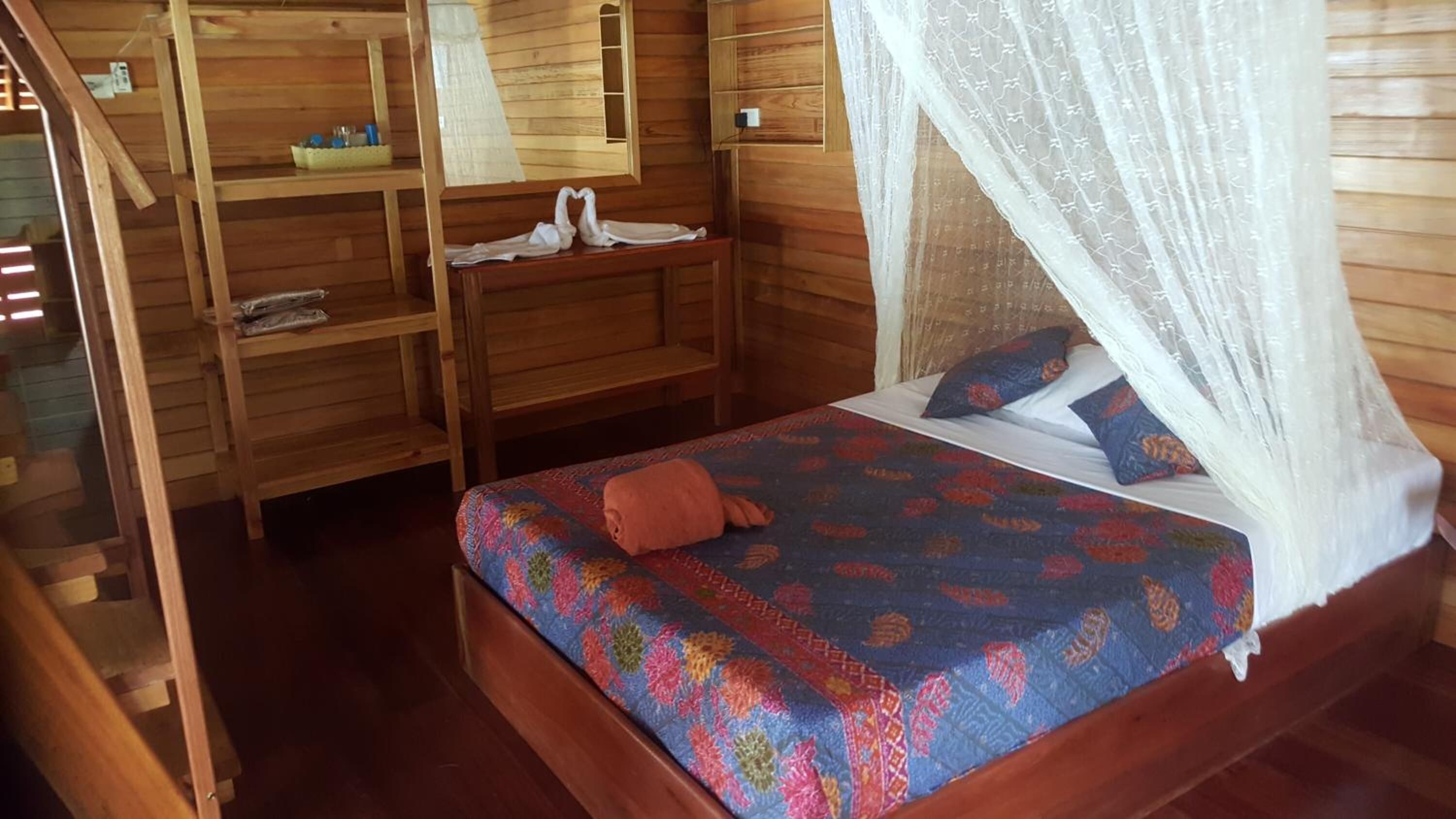A wooden room with a bed, a bench, and a shelf with items.
