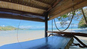 Un banco de madera con vistas a una playa, con una vista despejada del océano y colinas lejanas.