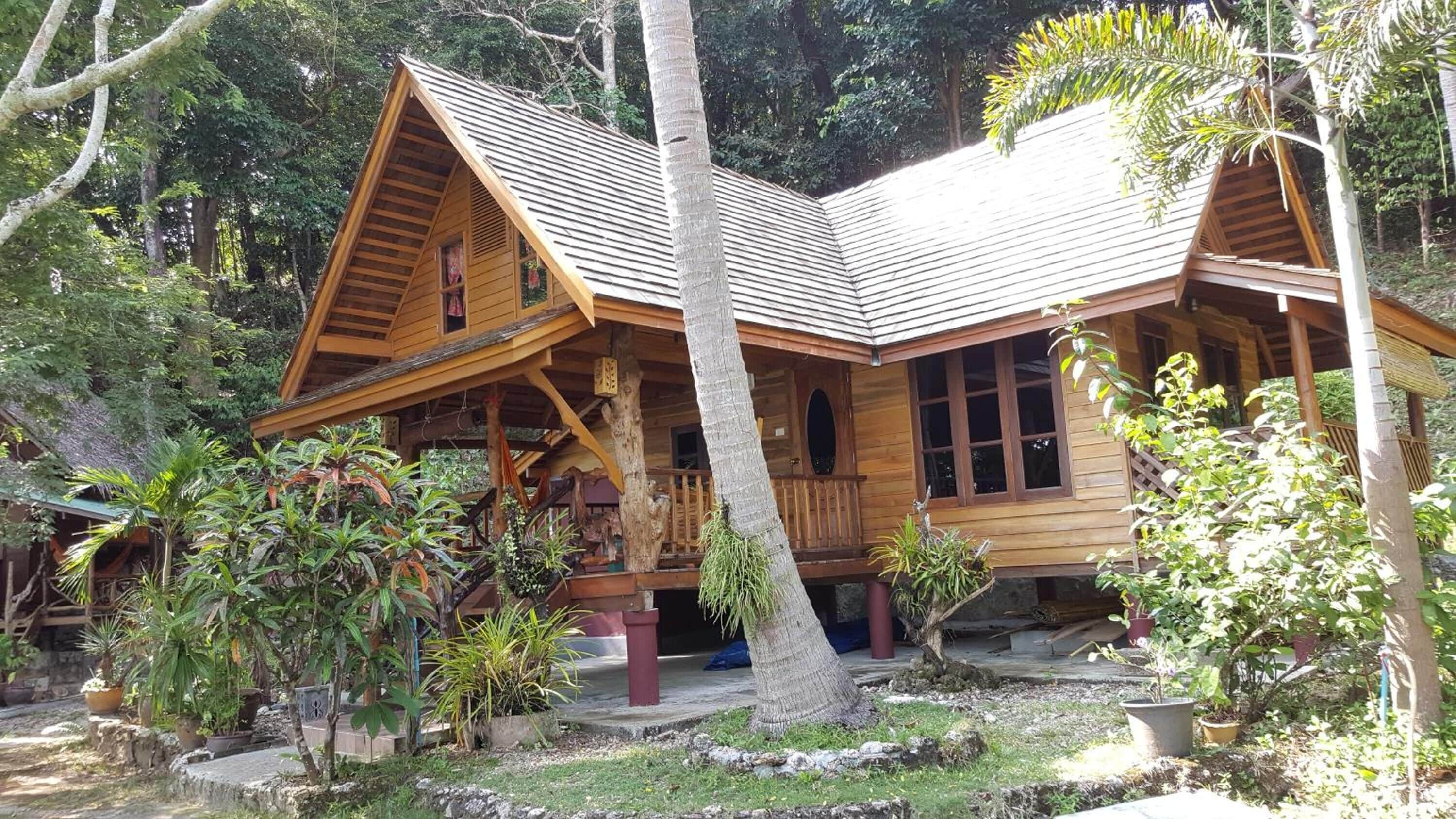 A wooden cabin with a sloped roof, surrounded by lush greenery and potted plants.