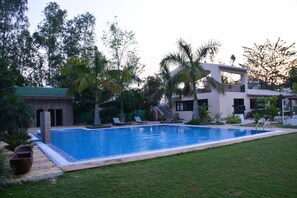 A swimming pool with a tiled deck, surrounded by a grassy area and palm trees. - Clarissa Resort (Ramnagar)