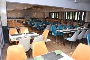 A spacious dining area with multiple tables and chairs, large windows, and a modern ceiling design. - Clarissa Resort (Ramnagar)