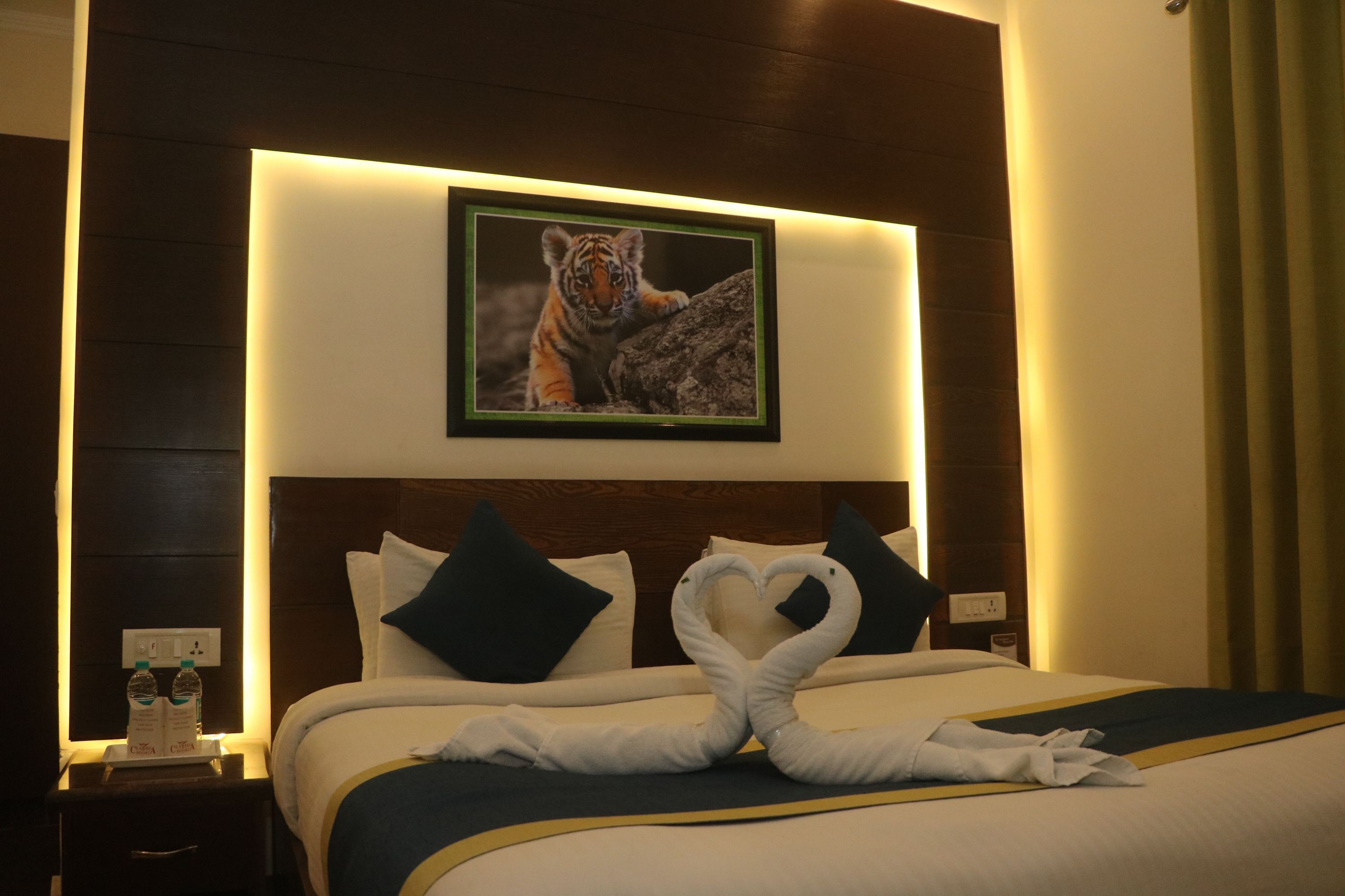 Habitación de hotel con cama, almohadas, un cuadro enmarcado de un tigre y una toalla dispuesta en forma de corazón.